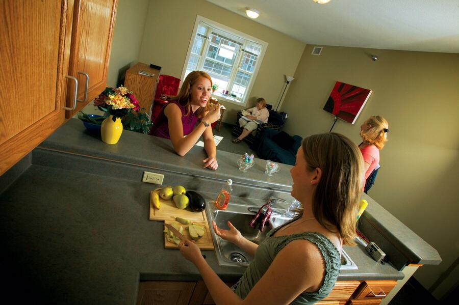 Young women hanging out in the kitchen and living room of a townhouse apartment.
